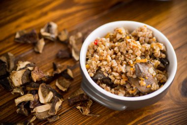 Haşlanmış karabuğday ve organik orman, kurutulmuş mantarlar ahşap bir masada seramik bir kasede.