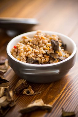 Haşlanmış karabuğday ve organik orman, kurutulmuş mantarlar ahşap bir masada seramik bir kasede.