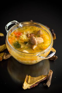 Siyah arka planda izole edilmiş cam bir kasede porcini mantarlı vejetaryen sebze çorbası.