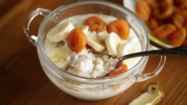 Masak oatmeal manis dengan aprikot kering dan pisang dalam mangkuk — Stok Video