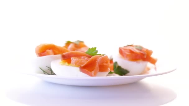 Helften van gekookte eieren met stukjes gezouten zalm op witte achtergrond — Stockvideo