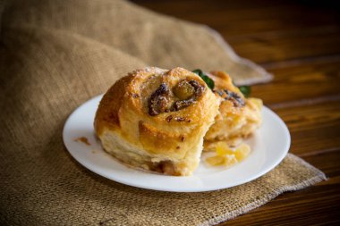 Reçelli tatlı kıvırcık çörek, tabakta pudra şekerli kuru üzüm.