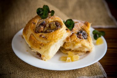 Reçelli tatlı kıvırcık çörek, tabakta pudra şekerli kuru üzüm.
