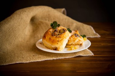 Reçelli tatlı kıvırcık çörek, tabakta pudra şekerli kuru üzüm.