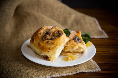 Reçelli tatlı kıvırcık çörek, tabakta pudra şekerli kuru üzüm.