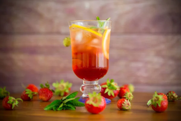 refreshing cool strawberry lemonade with lemon, ice and mint in a glass on a wooden table