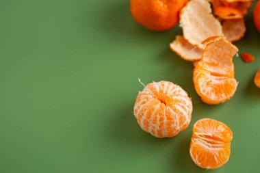Taze mandalinalar ve soyulmuş narenciye segmentleri yeşil zeminde.