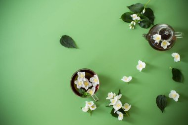 Yeşil arka planda cam bir kapta kokulu yasemin çayı.