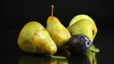 Siyah bir zemin üzerinde olgun armutlar ve erikler.