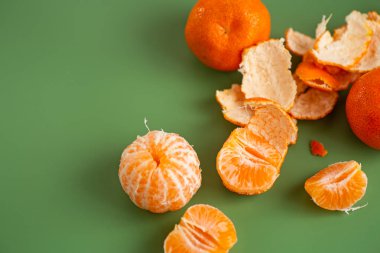 Taze mandalinalar ve soyulmuş narenciye segmentleri yeşil zeminde.