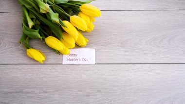 Tahta masada anneler günü tebrik kartı olan sarı lale buketi..