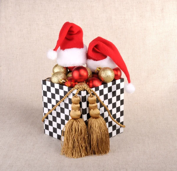 Geschenkbox im Dominostil, gefüllt mit Weihnachtskugeln. Hüte Weihnachtsmann. Dekoration aus Goldkordeln mit Quasten. — Stockfoto