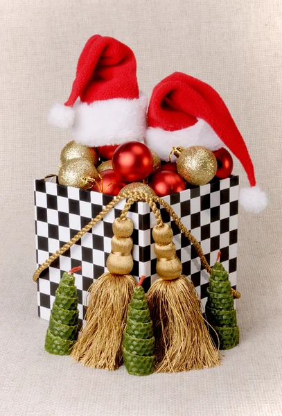 Gift box in a domino-style, filled with Christmas balls. Hats Santa Claus.Decoration made from gold cords with tassels. — Stock Photo, Image