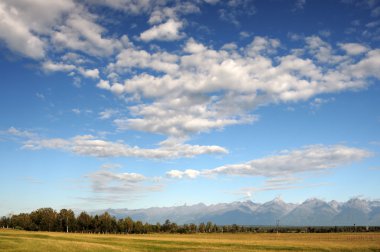 Mavi gökyüzü ve kümülüs bulutlar üzerinde Doğu Sayan Dağları ve Mount Munku-Sardyk. Kısmen renkli fotoğraf.