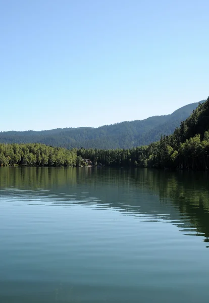 En el agua clara de un lago forestal refleja el cielo, la montaña, el bosque y las nubes. Foto parcialmente teñida . — Foto de Stock