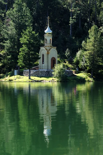 Iglesia ortodoxa rusa con una cúpula dorada en la orilla de un lago forestal rodeado de verde taiga. hermoso reflejo en el agua del lago . — Foto de Stock