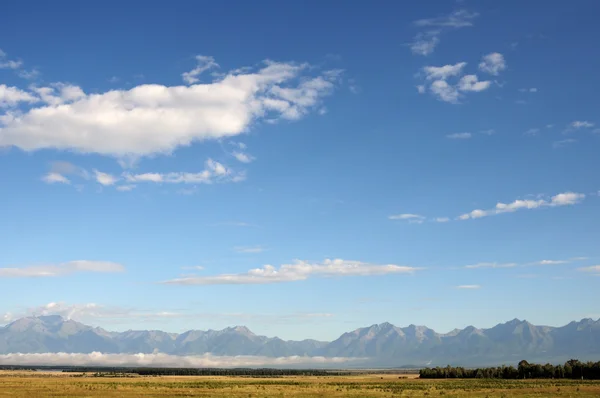 Ciel bleu et cumulus au-dessus des montagnes Sayan orientales et du mont MunKu-Sardyk. Photo partiellement teintée . — Photo