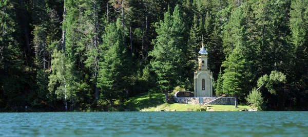 Iglesia ortodoxa rusa con una cúpula dorada en la orilla de un lago forestal rodeado de verde taiga. hermoso reflejo en el agua del lago . — Foto de Stock
