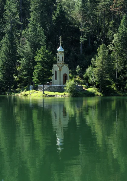 Iglesia ortodoxa rusa con una cúpula dorada en la orilla de un lago forestal rodeado de verde taiga. hermoso reflejo en el agua del lago . — Foto de Stock