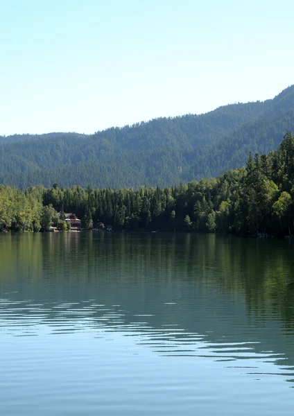 В чистой воде лесного озера отражаются небо, горы, лес и облака. Фото частично окрашено . — стоковое фото