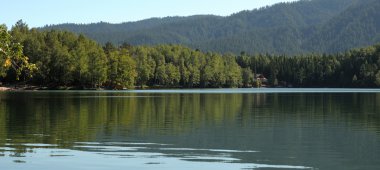 Bir orman göl temiz su gök, dağ, orman ve bulutlar yansıtır. Kısmen renkli fotoğraf.