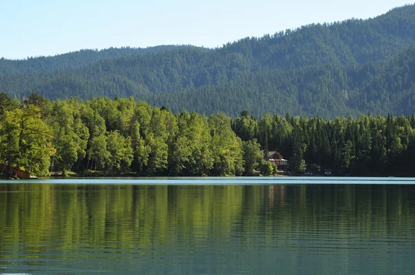 En el agua clara de un lago forestal refleja el cielo, la montaña, el bosque y las nubes. Foto parcialmente teñida . — Foto de Stock