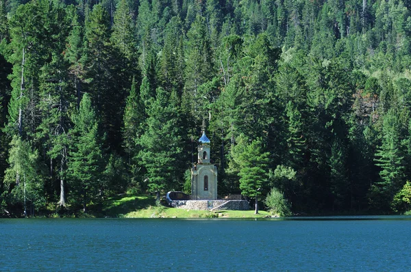 Iglesia ortodoxa rusa con una cúpula dorada en la orilla de un lago forestal rodeado de verde taiga. hermoso reflejo en el agua del lago . — Foto de Stock