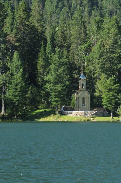 Iglesia ortodoxa rusa con una cúpula dorada en la orilla de un lago forestal rodeado de verde taiga. hermoso reflejo en el agua del lago . — Foto de Stock