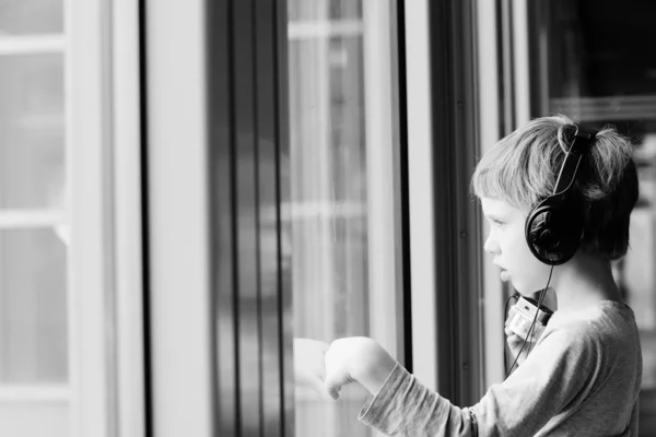 Chłopiec z słuchawki patrząc przez okno — Zdjęcie stockowe