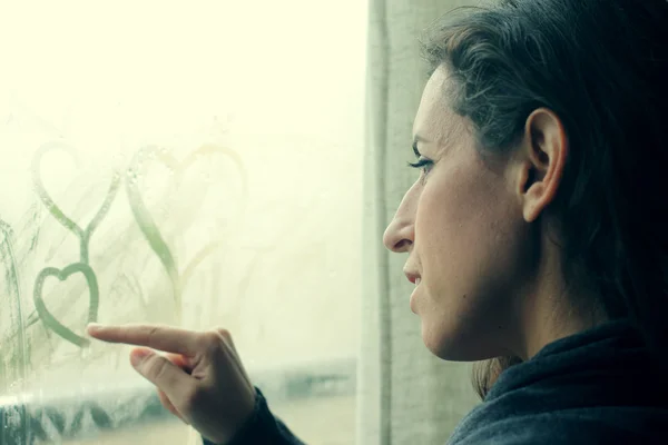Женщина рисует сердца на окне — стоковое фото