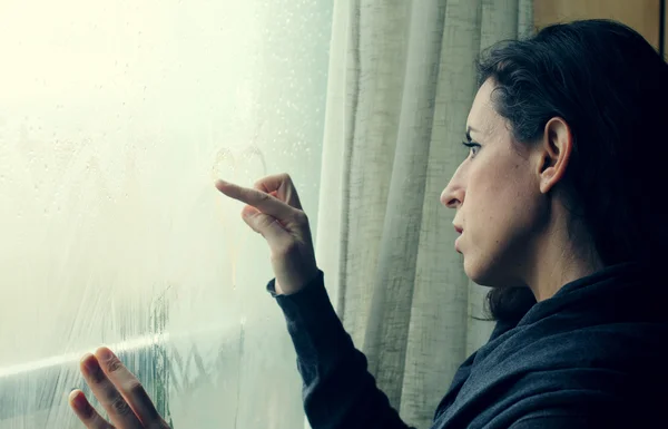 Frau zeichnet Herzen auf Fenster — Stockfoto