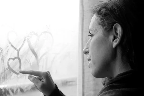 Woman drawing hearts on window — Stock Photo, Image