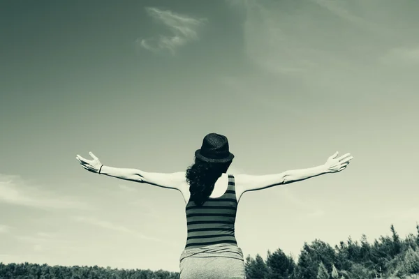 Ung kvinna tittar med öppna armar över himmel bakgrund — Stockfoto