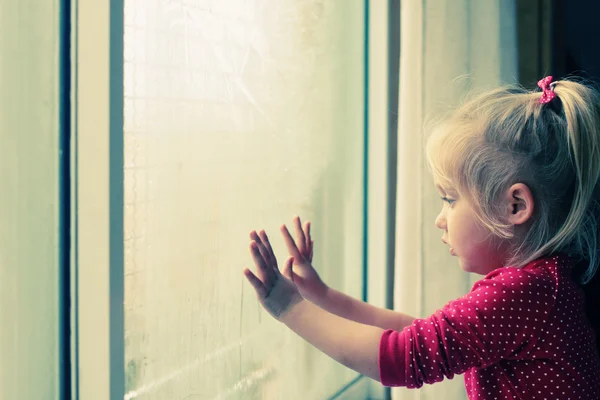 Little girl looking through window — Stock Photo, Image