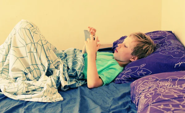 Boy lies in bed and plays — Stock Photo, Image