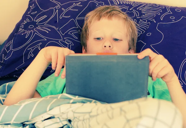 Boy lies in bed and plays — Stock Photo, Image