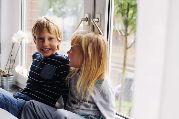 Hermana y hermano sentados cerca de ventana — Foto de Stock