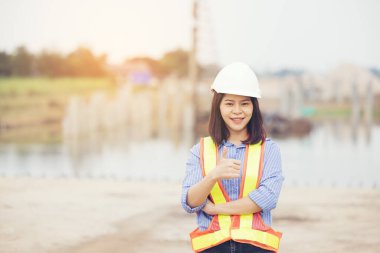 Miğferli kadın mühendis inşaat alanında baş parmağının iyi olduğunu gösteriyor. Kadınların gücü, cinsiyet eşitliği, çalışan kadınlar, kendinden emin kadın mühendis.