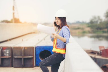 Beyaz şapkalı güzel Asyalı kadın mühendis ofis dışında inşaat alanında çalışıyor. Modern çalışan kadın otoyolu fikri.