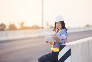 Beyaz şapkalı güzel Asyalı kadın mühendis ofis dışında inşaat alanında çalışıyor. Modern çalışan kadın otoyolu fikri.