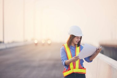 Beyaz şapkalı güzel Asyalı kadın mühendis ofis dışında inşaat alanında çalışıyor. Modern çalışan kadın otoyolu fikri.