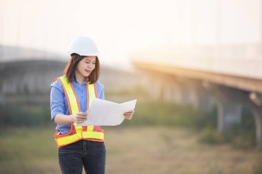 Beyaz şapkalı güzel Asyalı kadın mühendis ofis dışında inşaat alanında çalışıyor. Modern çalışan kadın otoyolu fikri.