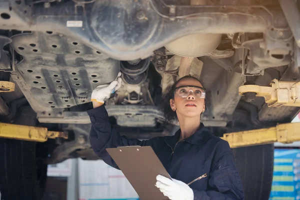 Female mechanic inspecting a lifted car