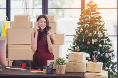 Gülümseyen genç bir kadın evde çalışıyor ve akıllı telefondan konuşuyor.