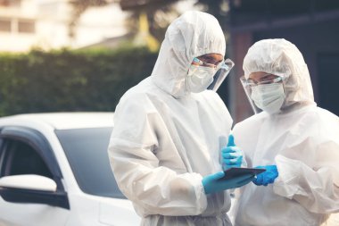 Pen giysili doktorlar sokakta dikilmeyi tartışan yüz kalkanıyla tablet kullanıyorlar.