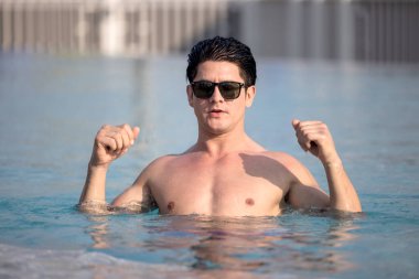 Yüzme havuzunun kenarında dinlenen güneş gözlüklü çekici genç adamın portresi.
