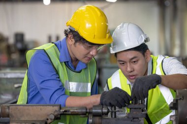 Üretim fabrikasında ekip olarak çalışan iki işçi, arka planda endüstri sahnesi, birlikte üretim faaliyetleri üzerinde çalışıyorlar.