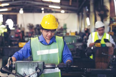 Üretim fabrikasında ekip olarak çalışan iki işçi, arka planda endüstri sahnesi, birlikte üretim faaliyetleri üzerinde çalışıyorlar.