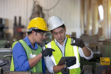 Üretim fabrikasında ekip olarak çalışan iki işçi, arka planda endüstri sahnesi, birlikte üretim faaliyetleri üzerinde çalışıyorlar.