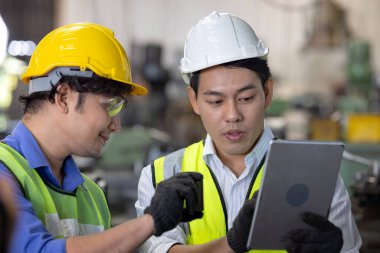 Üretim fabrikasında ekip olarak çalışan iki işçi, arka planda endüstri sahnesi, birlikte üretim faaliyetleri üzerinde çalışıyorlar.